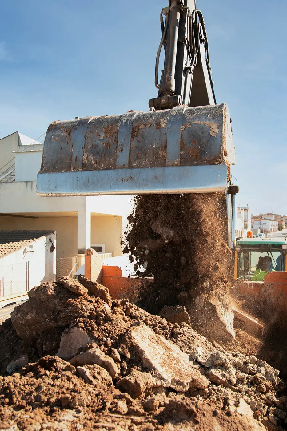 Ein Bagger arbeitet unter einem klaren blauen Himmel neben blühenden, gesunden Bäumen auf einer Baustelle.